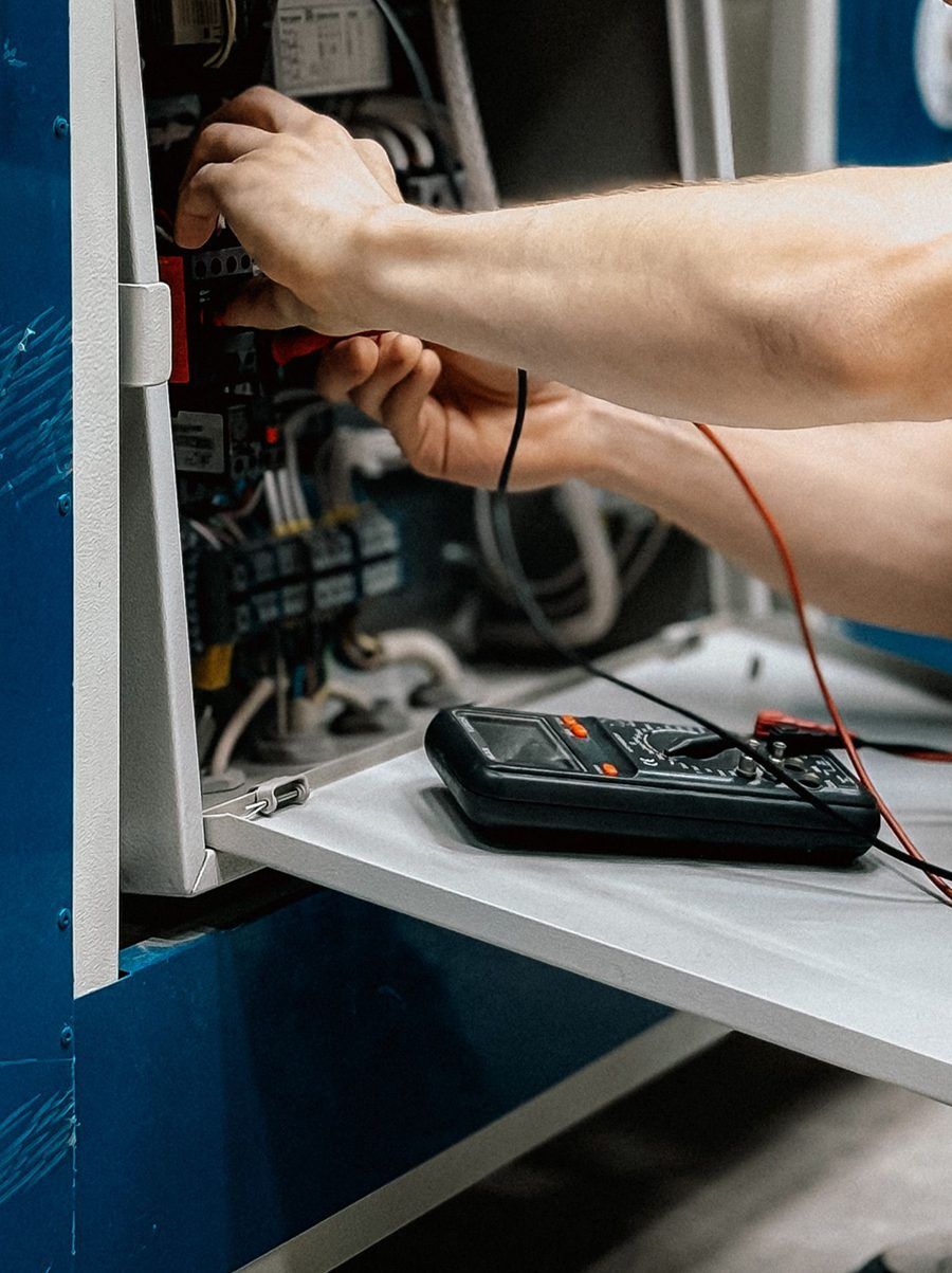 Mains d'un technicien branchant des câbles dans un appareil ouvert, un multimètre posé sur la tablette