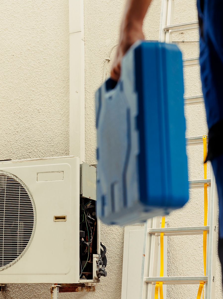 Technicien portant une mallette d'outils bleue devant une unité extérieure de climatisation